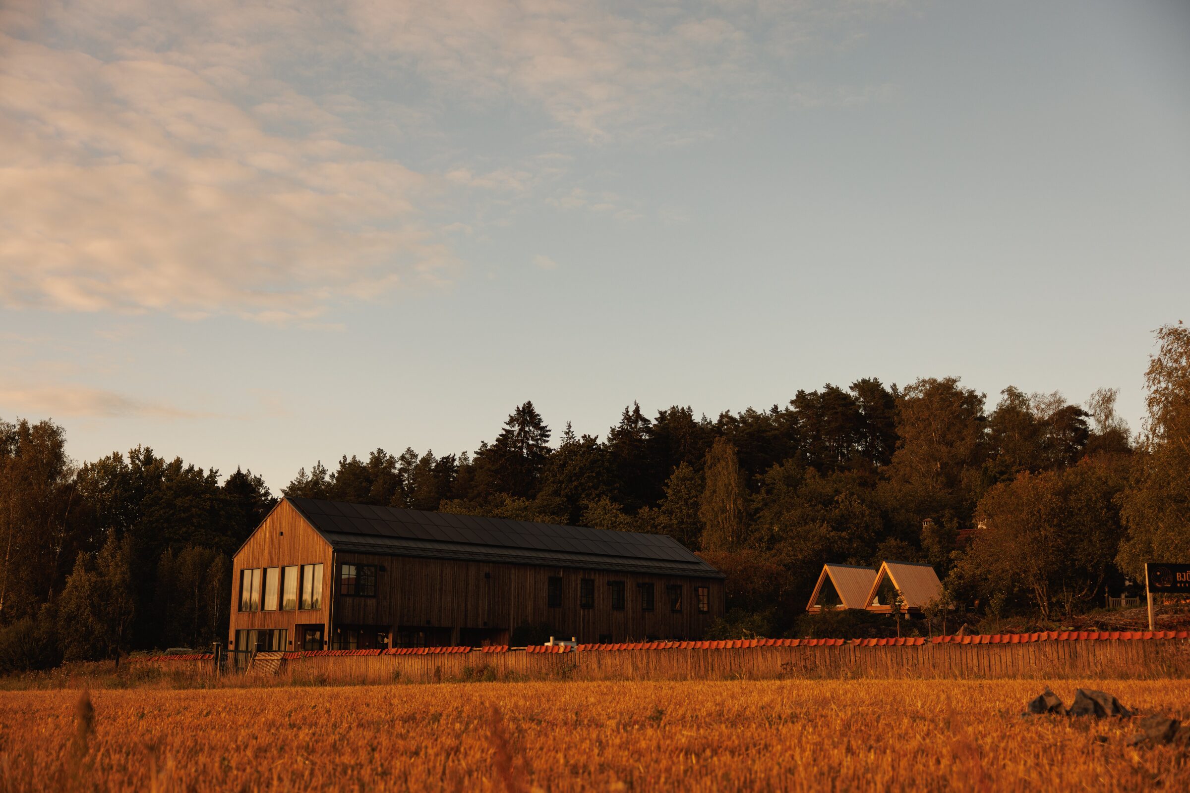 Björnbacka at golden hour — main hall and A-frame cabins at the edge of the forest