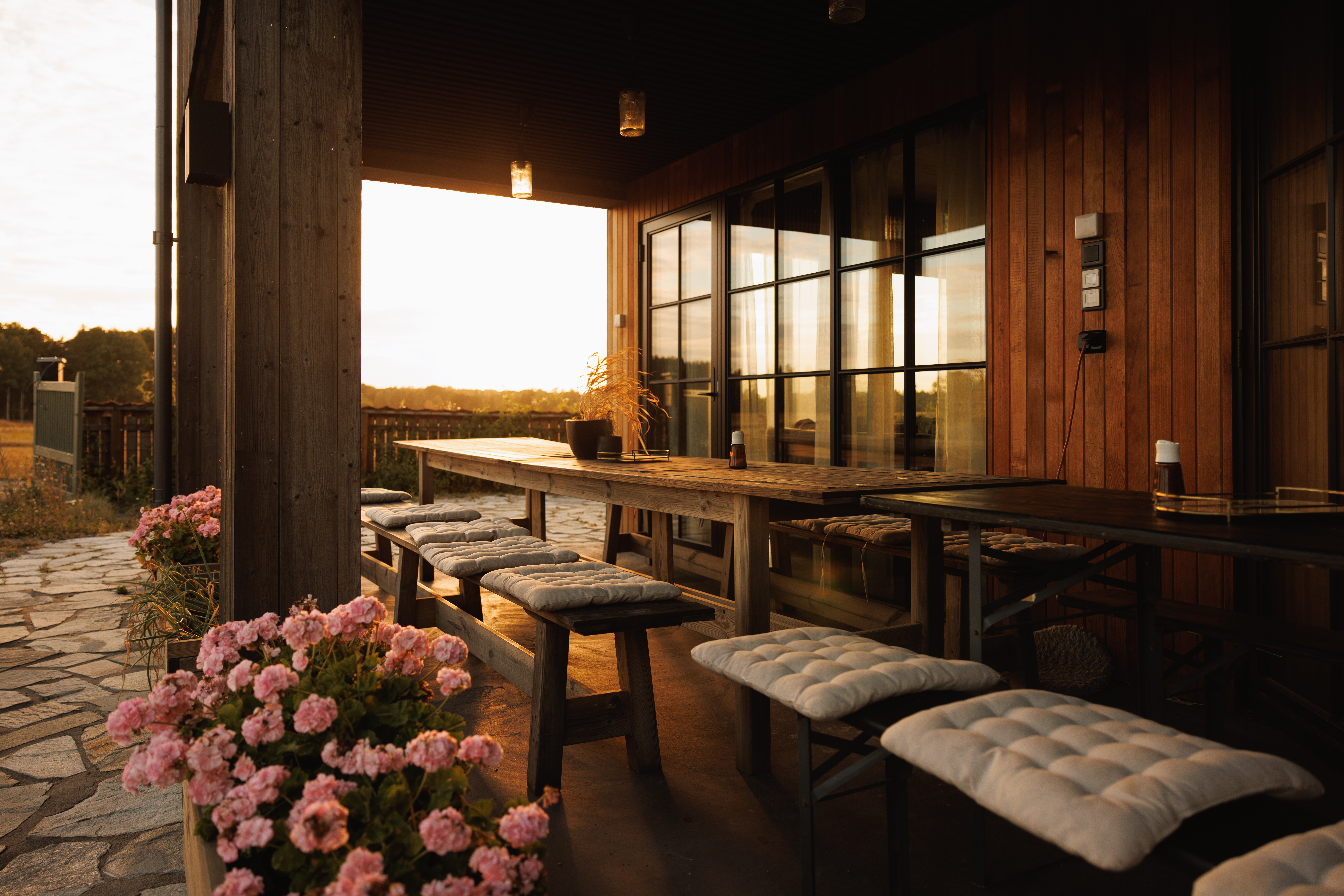 Golden-hour terrace at Björnbacka with wooden benches, cushions, and flowers at sunset